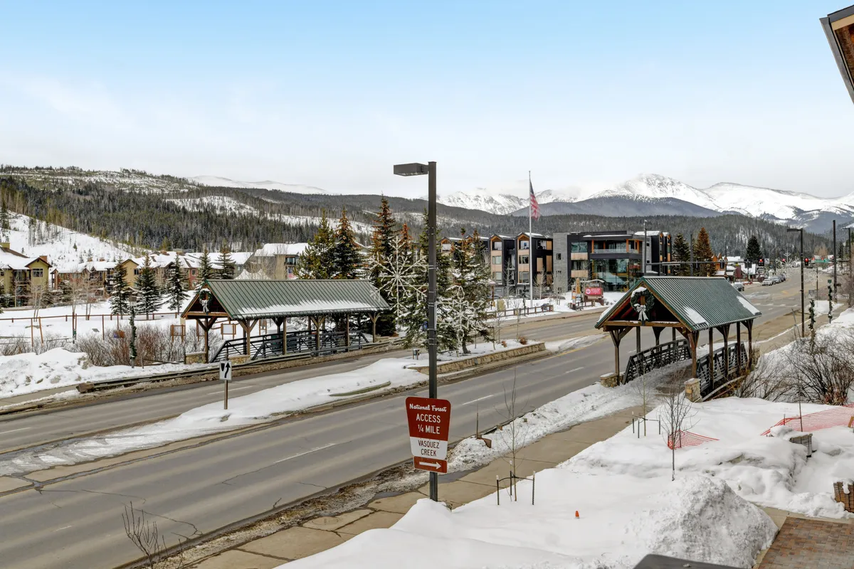 A panoramic view of snow-covered mountains rising behind Winter Park’s main street, with transportation shelters, buildings, and a tranquil atmosphere. The early morning light suggests the start of a day filled with outdoor adventure.