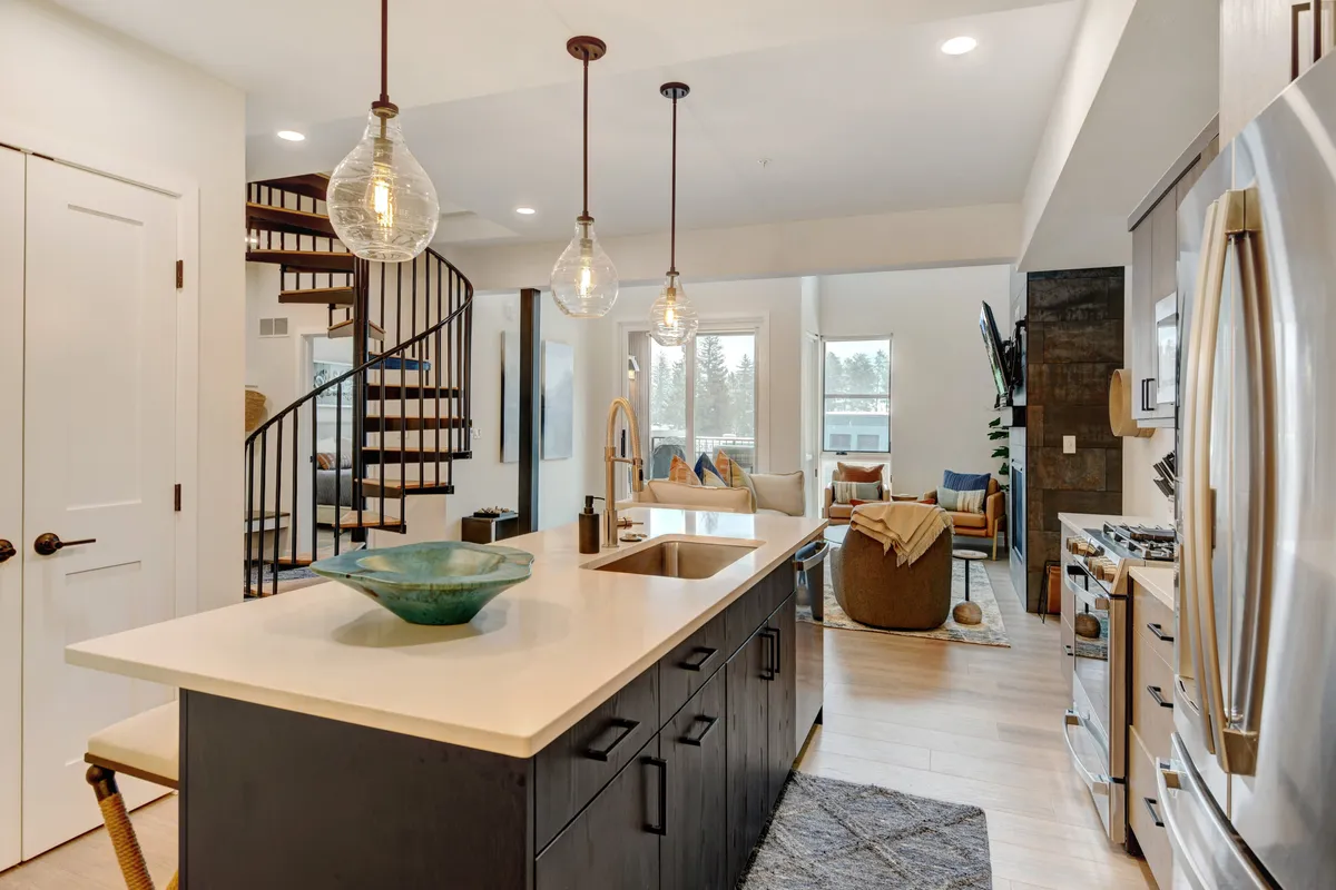 A contemporary open-concept area with a kitchen island, a spiral staircase, a living space with comfortable seating, and expansive windows that let in abundant natural light.