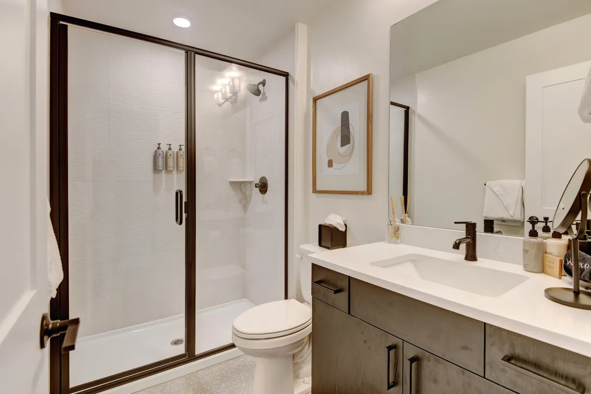 A modern bathroom featuring a glass shower enclosure, a vanity with a sink, and stylish framed artwork. The space feels fresh, serene, and spa-like, with premium finishes designed for relaxation and self-care.