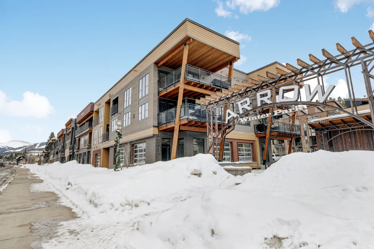 An exterior shot featuring the modern 'ARROW' building, with snow covering the surroundings. People are seen walking, skiing, and exploring nearby shops, capturing the energy and activity of the neighborhood during winter. The image hints at both outdoor adventure and community events.