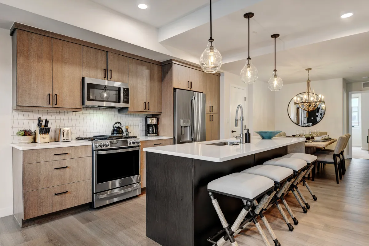 This image features a spacious chef’s kitchen with a large kitchen island, modern stainless steel appliances, pendant lighting, and an adjoining dining area. The scene is warm, inviting, and perfectly suited for both cooking and entertaining, highlighting ample prep spaces and a sociable atmosphere.