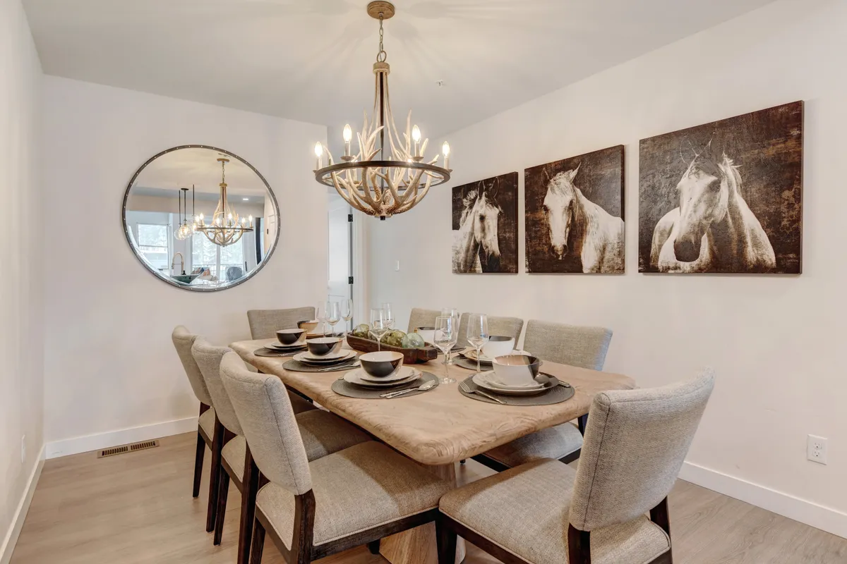 A sophisticated dining area featuring an elegant dining table set beneath a chandelier, with striking horse artwork and a mirror enhancing the cozy, welcoming ambiance. The table is arranged for family gatherings or memorable dinners.
