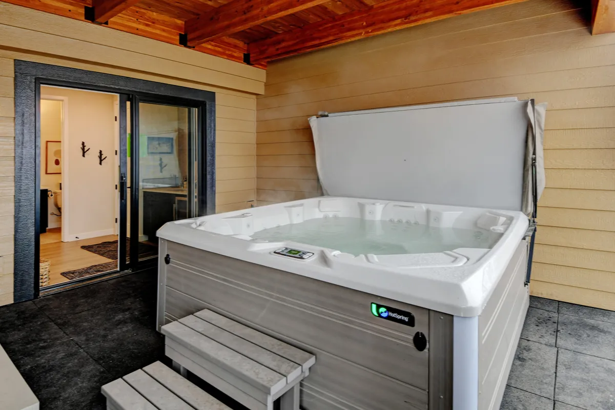 This exterior shot features a private hot tub set against a backdrop of wooden beams and a sliding glass door, offering a tranquil outdoor space perfect for relaxation after a day of activities. The scene captures the essence of resort-style pampering and privacy.
