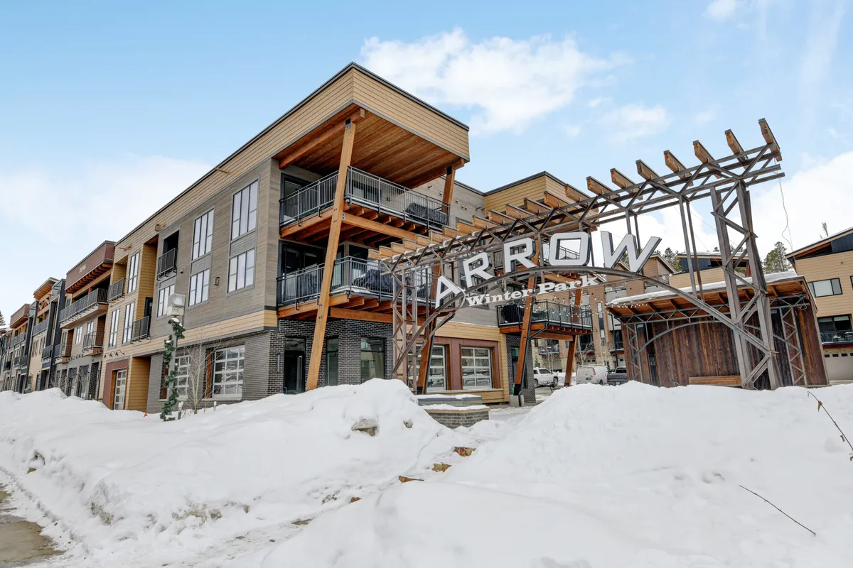 An exterior perspective featuring the modern ARROW Winter Park sign, snow-covered ground, and contemporary architecture, with spectacular mountain views hinting at proximity to outdoor adventures and downtown amenities.