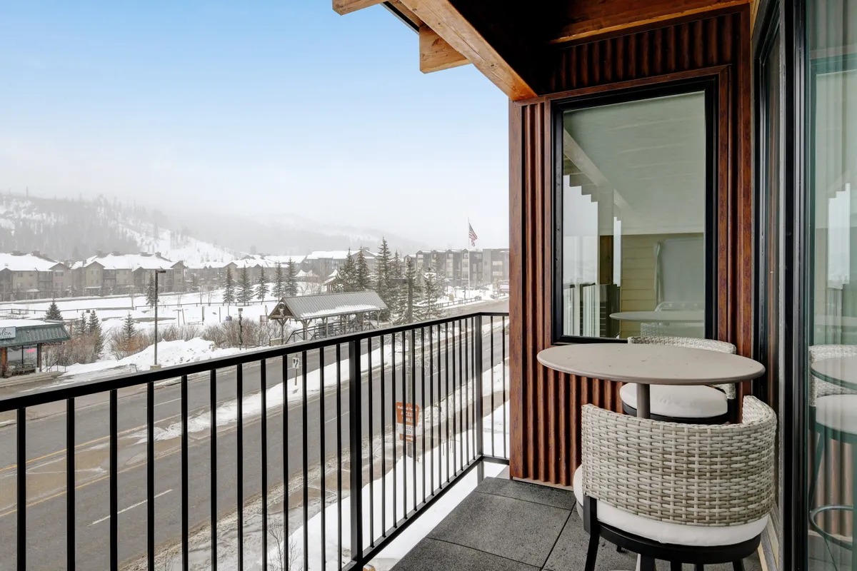 This image captures a balcony with comfortable seating overlooking a beautiful, snow-covered mountain landscape. The tranquil scene shows the ideal spot for sipping morning coffee, unwinding with friends, or enjoying the crisp mountain air before heading out for the night.